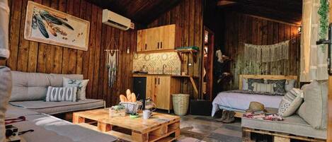 Ein rustikales Blockhaus-Interieur mit Holzwänden, Holzbalkendecke, einer Couch, einem Bett, einem Couchtisch und einer Hängelampe.