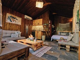 Interior rústico de una cabaña con paredes y techo de madera, un sofá, una cama, una mesita de centro y un colgador de luz.