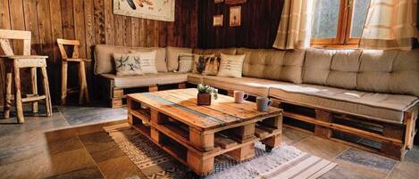 A rustic cabin interior with a wooden sofa, a wooden coffee table, and a large window with curtains.