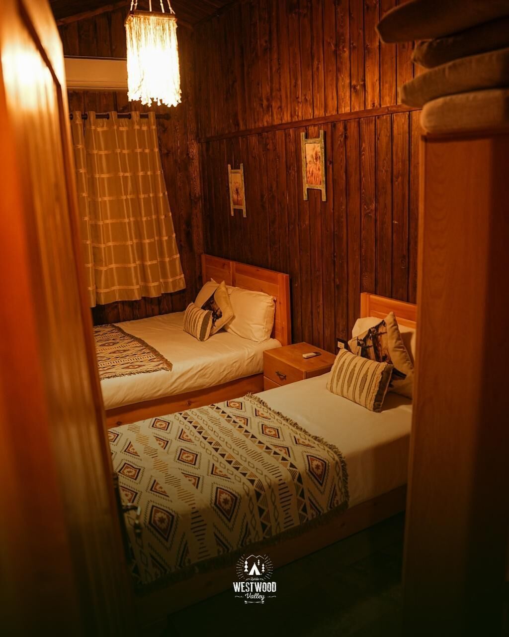 Una habitación acogedora con dos camas, paredes de madera y una lámpara colgante.
