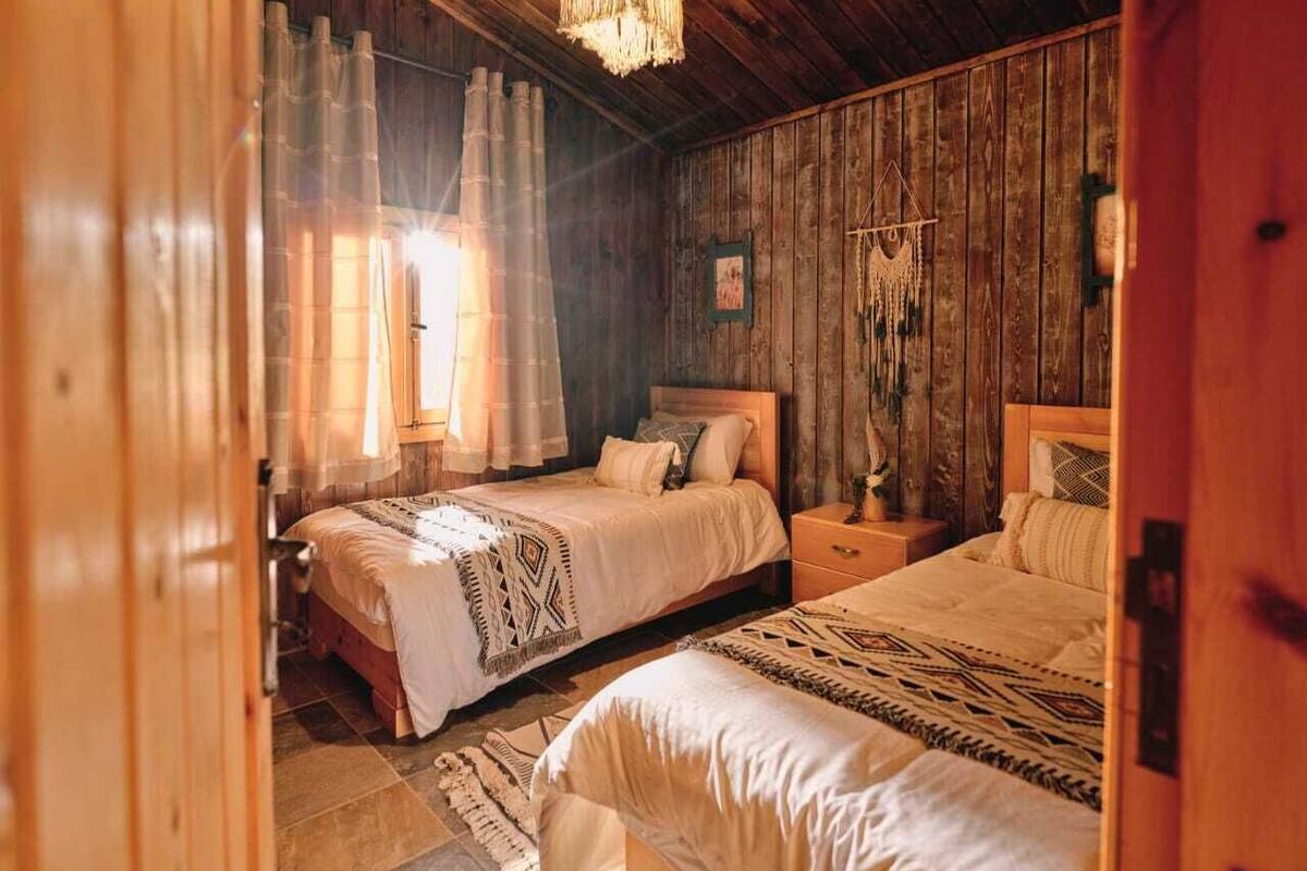 Une pièce chaleureuse en bois, avec deux lits, un luminaire suspendu et une décoration rustique.