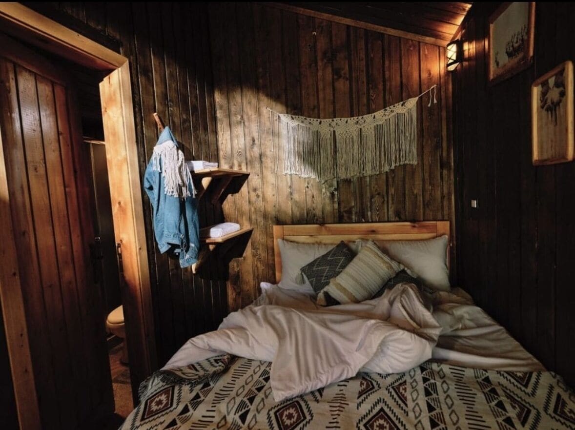 Una habitación rústica de madera con una cama, una lámpara colgante y una puerta de madera.