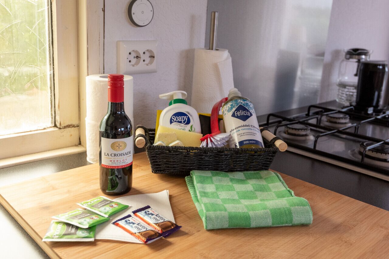 A kitchen counter with a bottle of wine, a basket of toiletries, and a green checkered cloth.