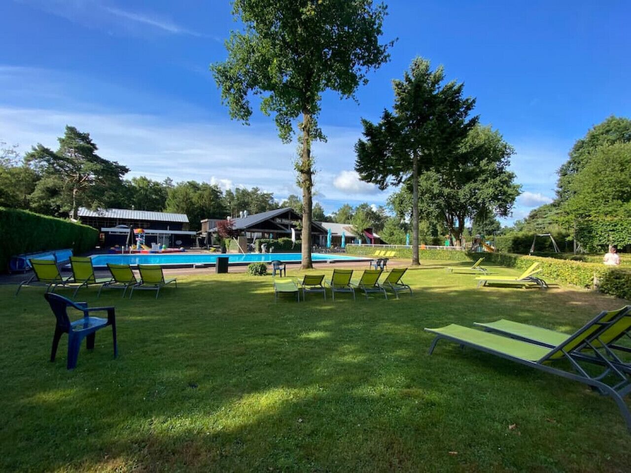 Un espacio con césped, varias sillas de descanso y una piscina.