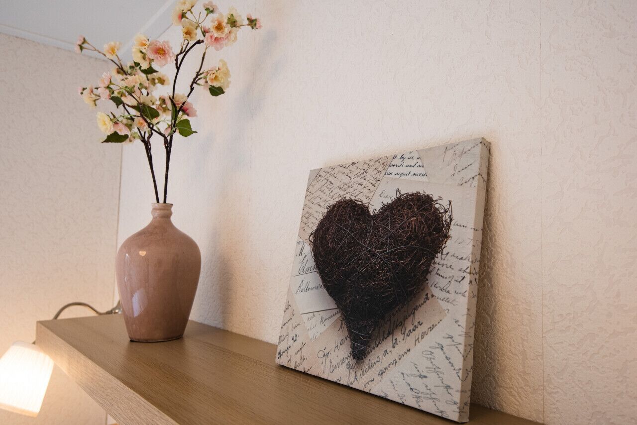 A vase with flowers and a framed picture with a heart design on a wooden surface.