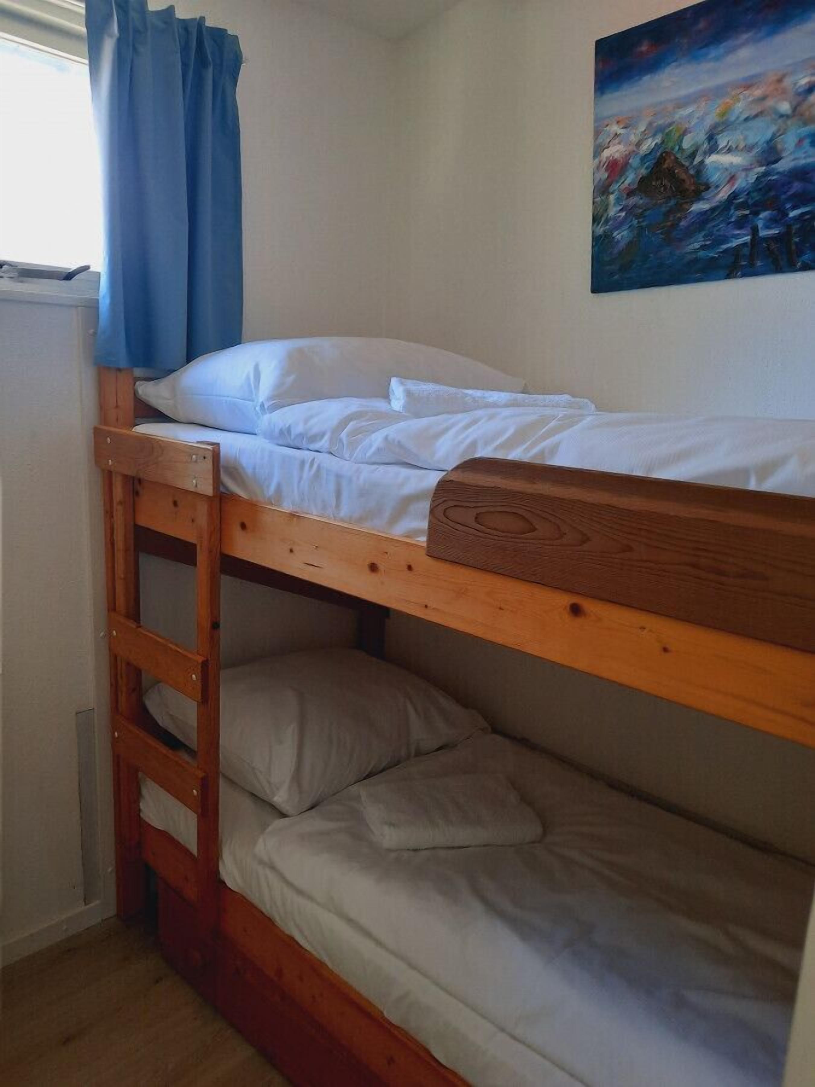 Habitación con literas, una escalera de madera, ropa de cama blanca y un cuadro en la pared.
