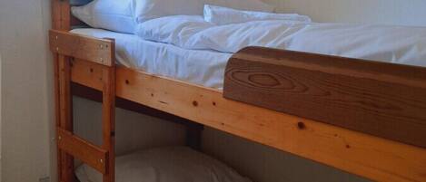 Habitación con literas, una escalera de madera, ropa de cama blanca y un cuadro en la pared.