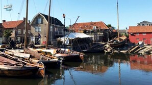 Un port où des bateaux sont amarrés, un bâtiment avec un toit rouge et une tente sur l’eau.