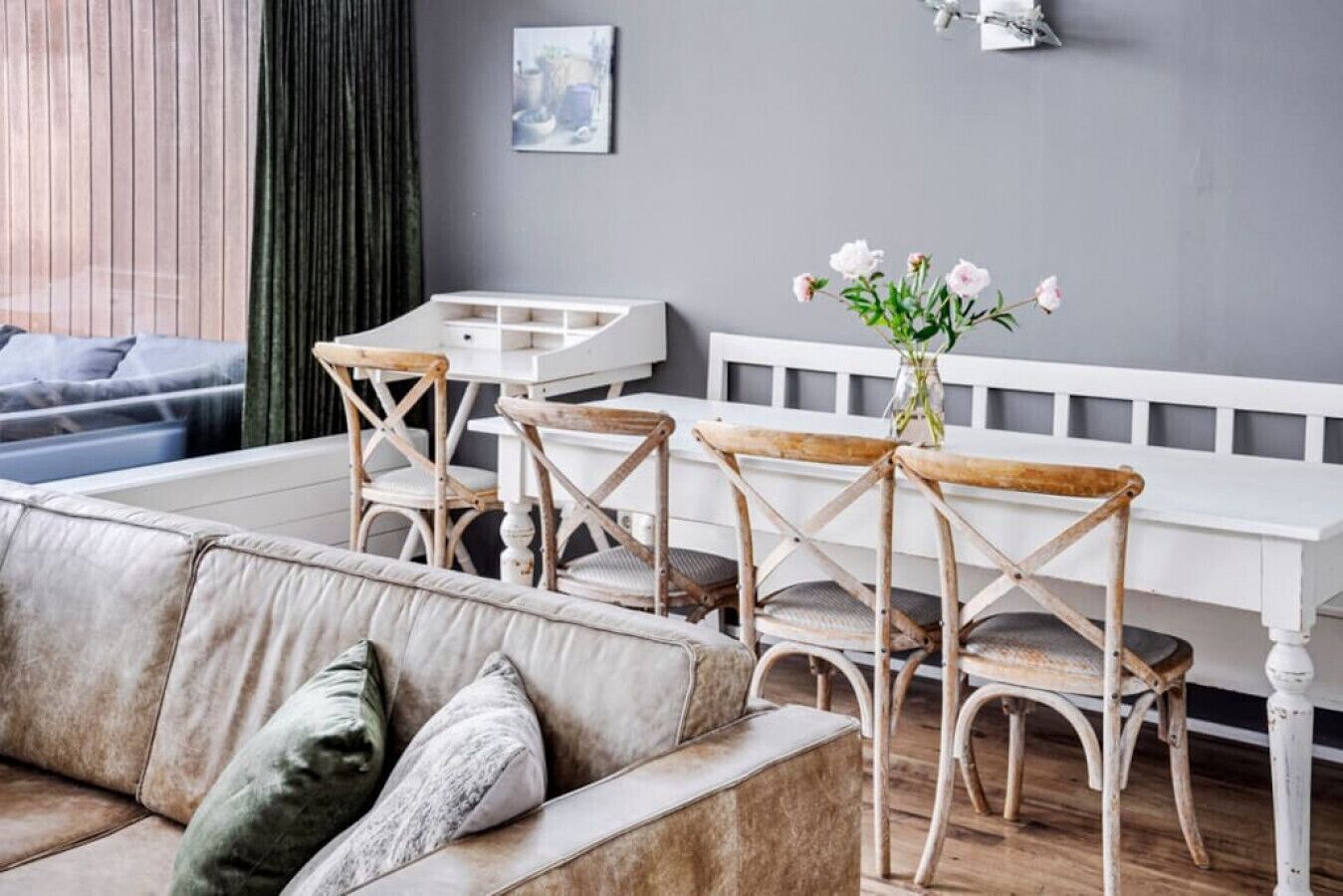 Een gezellige woonkamer met een beige bank, houten stoelen, een witte tafel en een bloemenvaas.