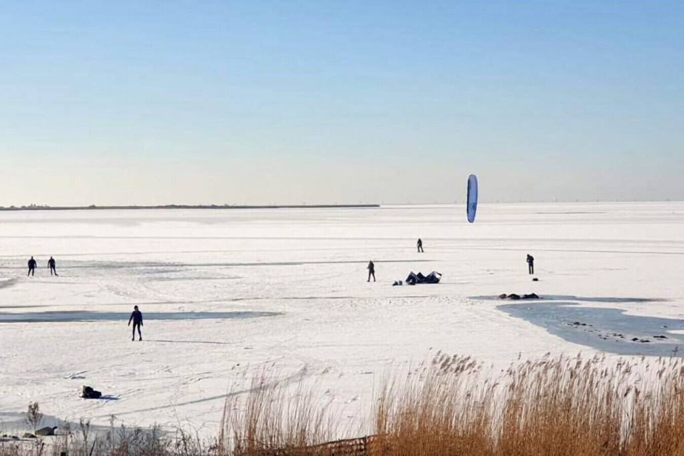 Paisatge nevós i extens, amb persones participant en activitats a l'aire lliure, possiblement relacionades amb un objecte blau gran.