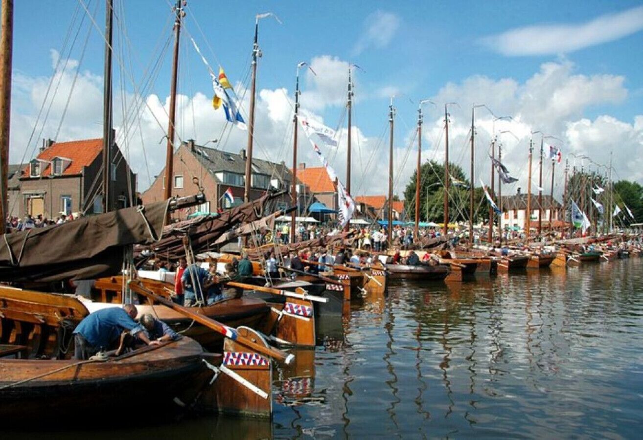 A marina with numerous wooden boats docked, a clear sky, and buildings in the background.