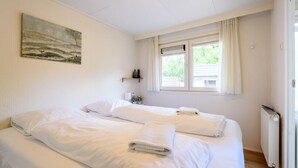 Ein Schlafzimmer mit zwei Betten, einem Fenster mit Vorhängen, einem Heizkörper und einem Bild an der Wand.