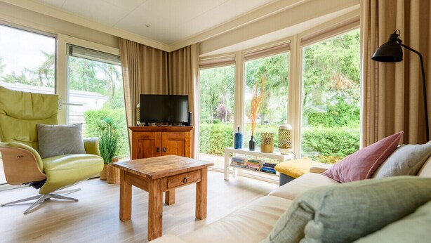 Ein geräumiges Wohnzimmer mit großem Fenster, einem Holztisch, einer Couch und einem Fernseher.