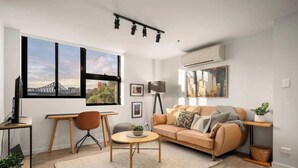 A modern living room with a sofa, a round coffee table, a desk with a chair, and a large window with a city view.