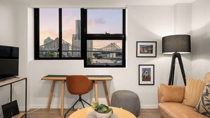 A modern living room with a large window, a desk, a TV, a sofa, and a lamp.