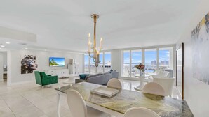 A modern living room with a dining area, large windows, and a city view. - 39th Floor Apt | Hot Tub | Gym | StayCozy (Miami)
