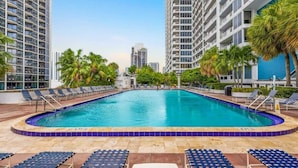A swimming pool surrounded by lounge chairs and palm trees, with high-rise buildings in the background. - Central Long Stay Base | Gym & Balcony | StayCozy (Miami)