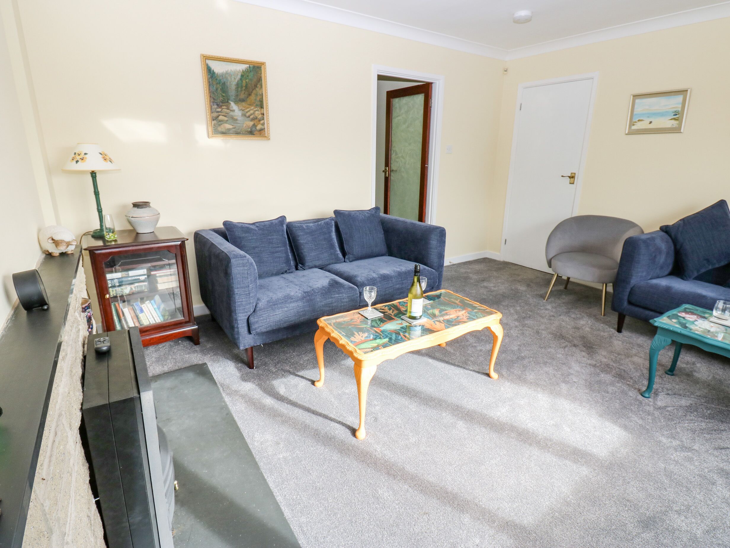 A living room with a blue sofa, a wooden coffee table, a bookshelf, and a door.