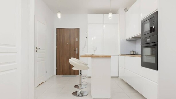 Een moderne keuken met witte kasten, een houten deur, een witte barstoel en ingebouwde apparatuur.