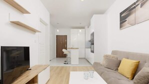 Een moderne woonkamer met een flatscreen televisie, een witte salontafel en een beige bank met een geel kussen.