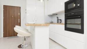 Een moderne keuken met witte kasten, een houten deur, een witte barstoel en twee zwarte ovens.
