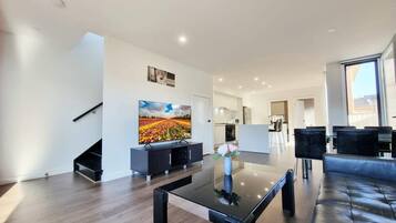 A modern living room with a flat-screen TV, a glass coffee table, and a sofa. There is a staircase leading to another level.