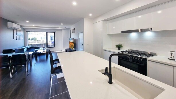 Una cocina moderna con armarios blancos, una isla central y un área de comedor con sillas negras.