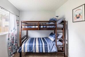 Una cama litera con ropa de cama a rayas, una ventana con cortina floral y un cuadro en la pared.