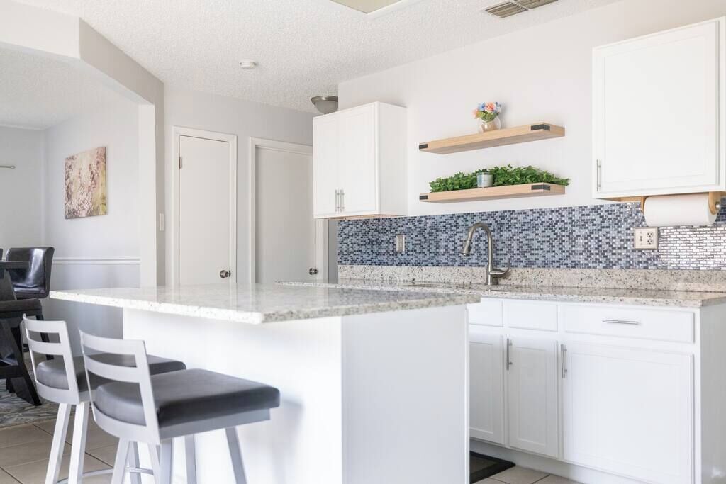 Eine moderne Küche mit weißen Schränken, einer Granit Arbeitsplatte und einer Rückwand mit blauen Mosaikfliesen.