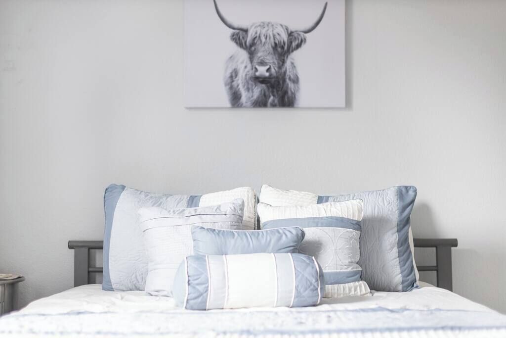 Een slaapkamer met een bed, kussens en een schilderij van een stier.