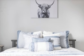 A bedroom with a bed, pillows, and a wall-mounted artwork of a bull.