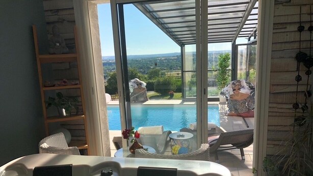 A hot tub with a view of a swimming pool and outdoor seating area.