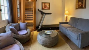 A living room with a treadmill, grey sofa, wicker chairs, and a lamp.