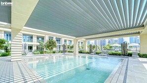 A modern hotel pool area with a clear pool, sunshade structures, and a view of the city skyline. - bnbme | Burj Royale | 1 BDR (Dubai)