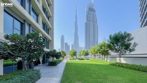 A modern hotel courtyard with a pathway, green lawn, and trees. - bnbme | Burj Royale | 1 BDR (Dubai)