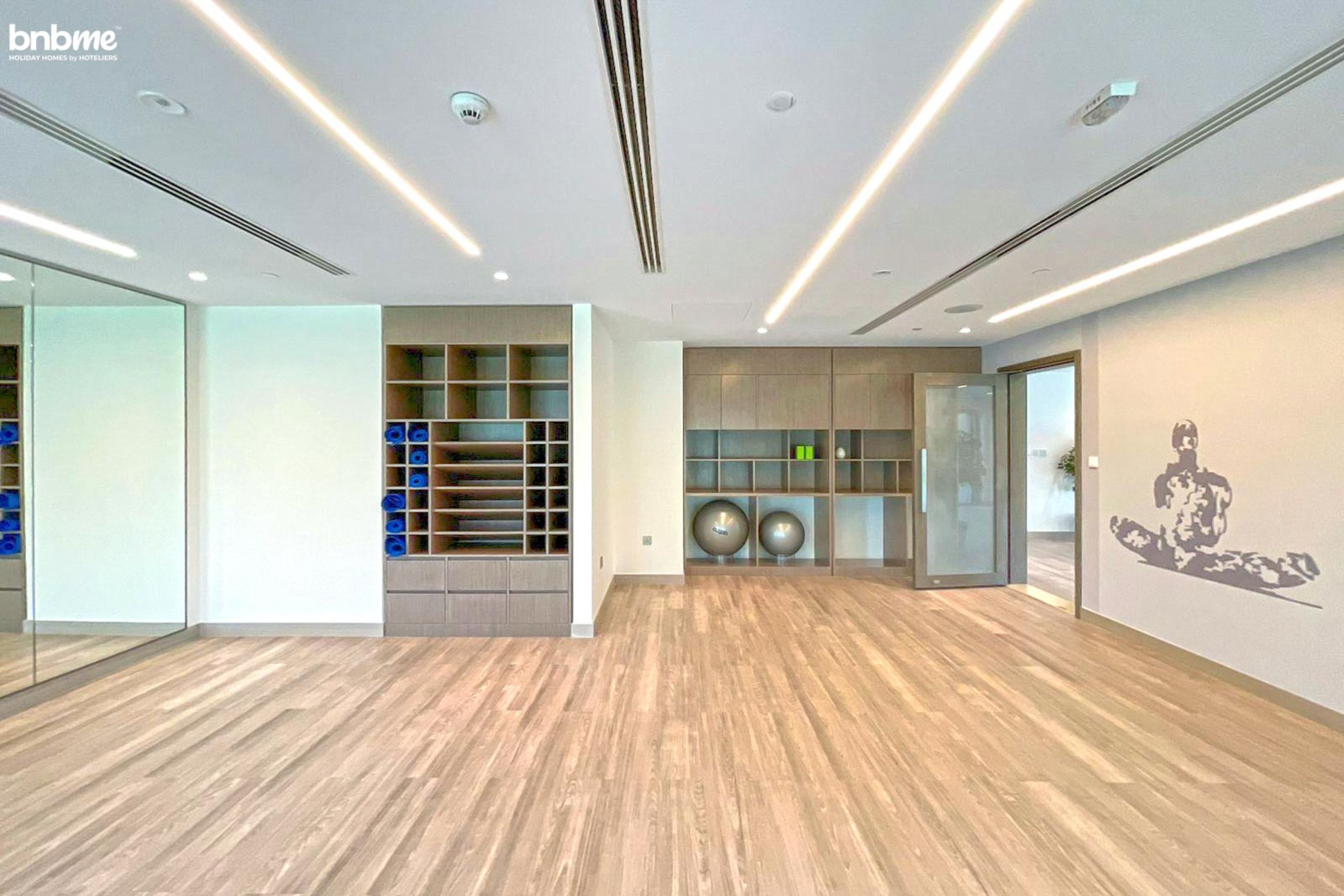 Una habitación amplia con suelo de madera, estanterías empotradas, una puerta de cristal y una escultura fijada a la pared.