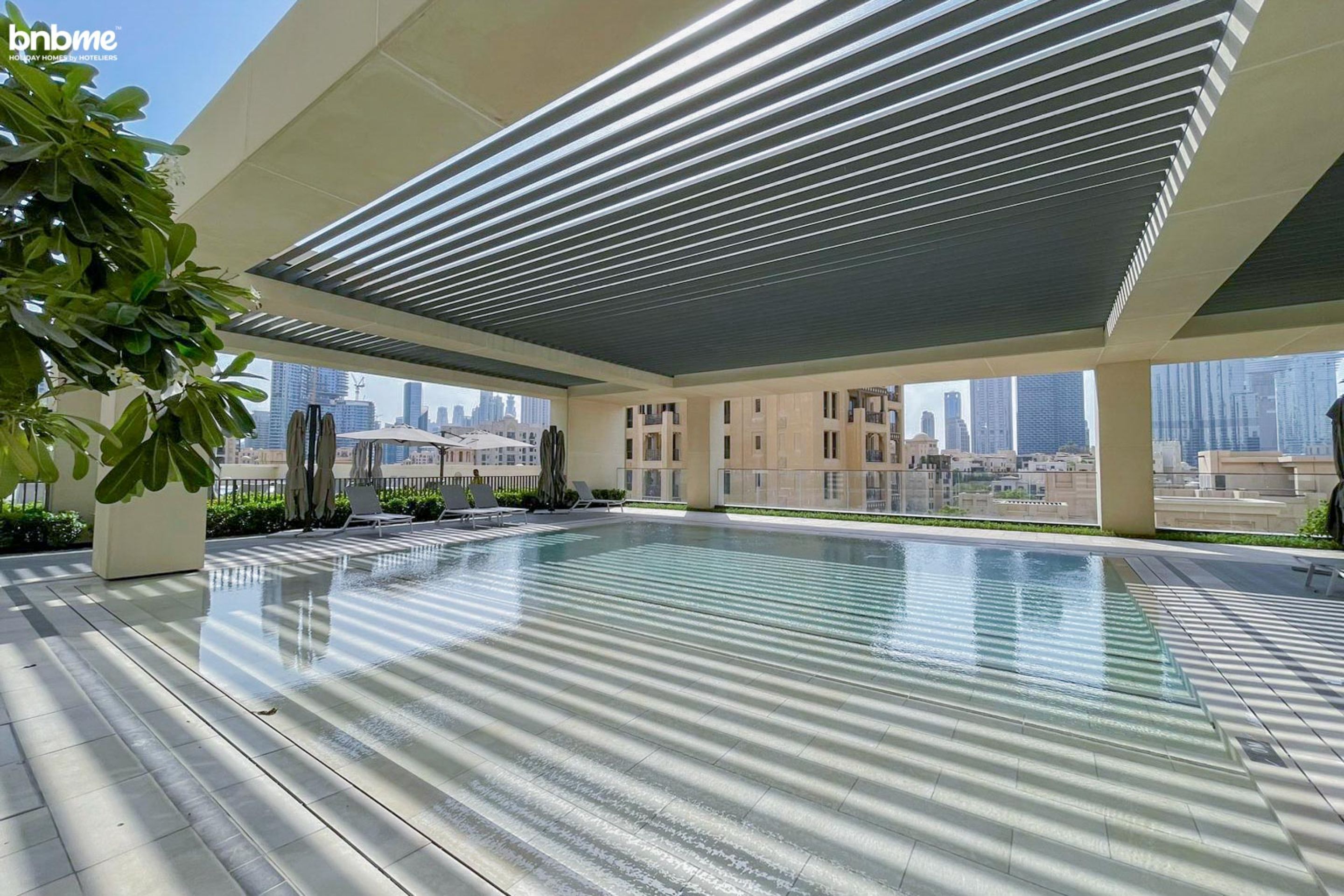 Une piscine sur le toit, offrant une vue sur les gratte-ciel de la ville, entourée d’une architecture moderne et de plantes en pot.