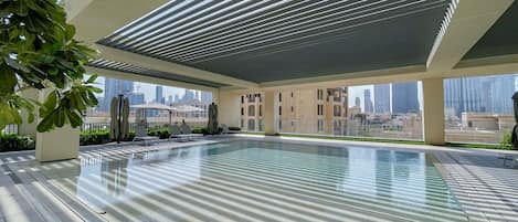 Una piscina en la azotea con vistas al horizonte de la ciudad, rodeada de arquitectura moderna y plantas en macetas.