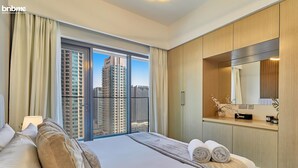 A modern hotel room with a large bed, a vanity with a mirror, and a view of tall buildings. - bnbme | Burj Royale | 1 BDR (Dubai)