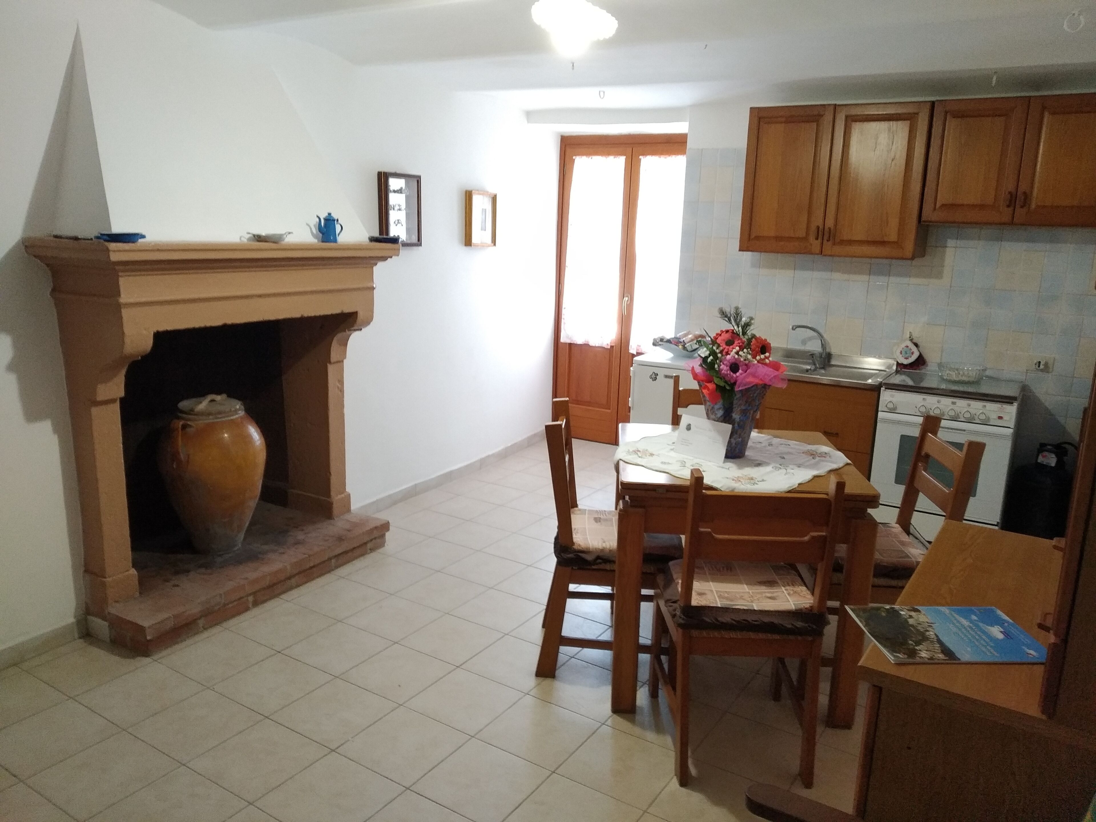A kitchen with a tiled floor, wooden cabinets, a stove, and a dining area with chairs and a table.