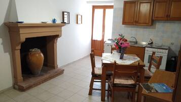 A kitchen with a tiled floor, wooden cabinets, a stove, and a dining area with chairs and a table.