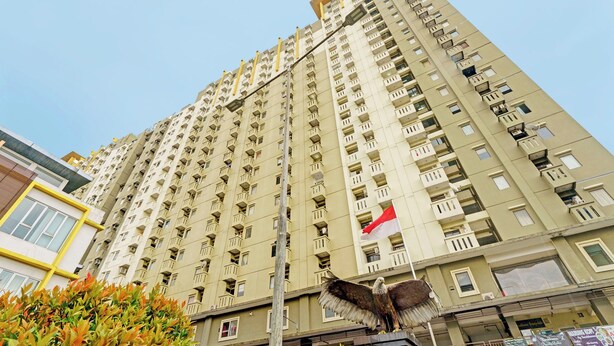 Un edificio de gran altura con varios balcones, una bandera y follaje circundante.