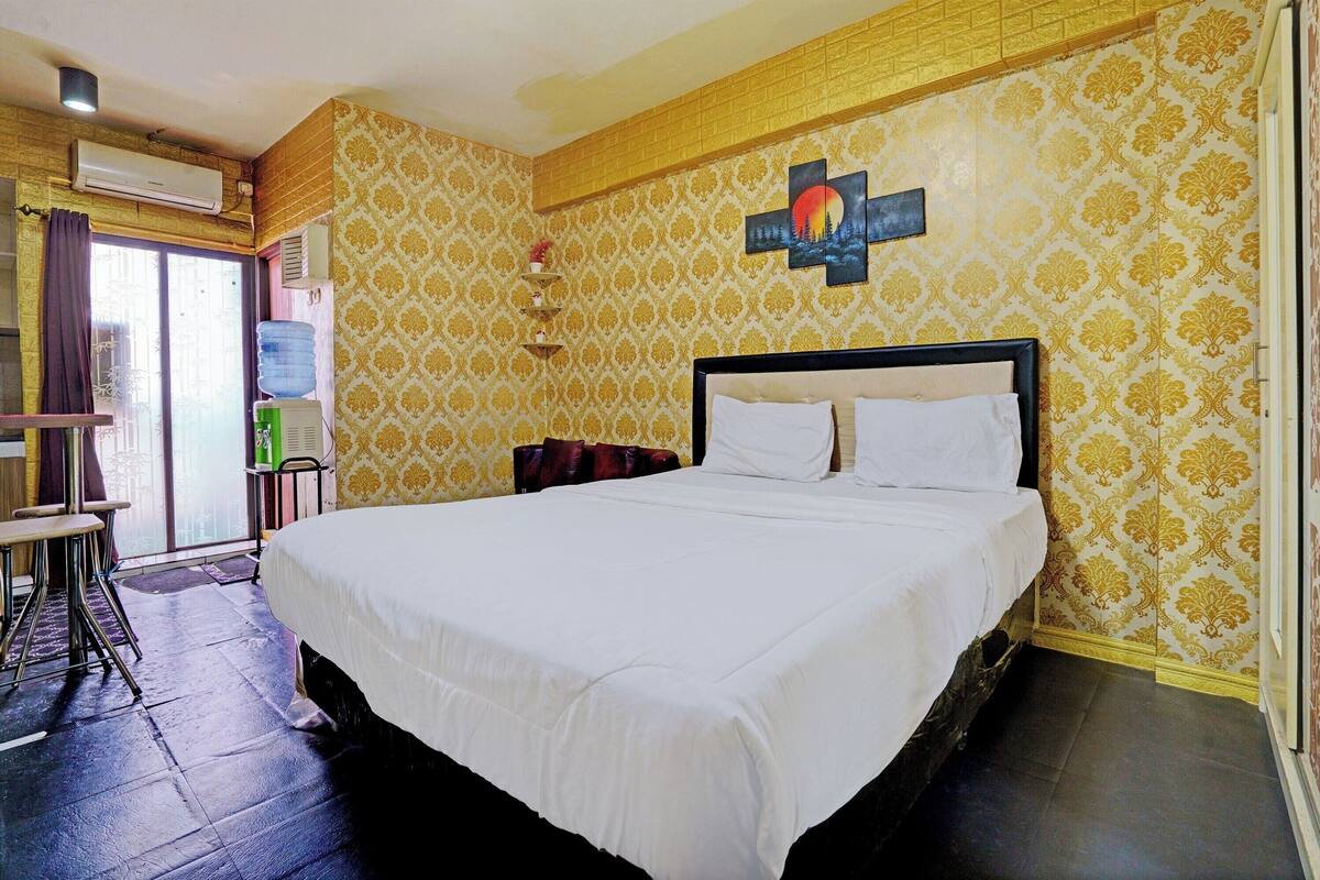 Une chambre d’hôtel avec un grand lit, un bureau et une chaise. Elle est équipée d’une fenêtre avec des rideaux, d’un distributeur d’eau et d’un climatiseur.
