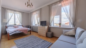A bedroom with a bed, a TV, a sofa, a desk, and a window with curtains. - Luxurious apartment  in Minsk (Minsk)