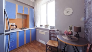A compact kitchen with blue cabinets, a refrigerator, a coffee maker, and a window with curtains. - Luxurious apartment  in Minsk (Minsk)