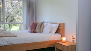 Un dormitorio con cama de madera, ropa de cama blanca y una mesita de noche con lámpara.