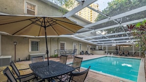 An outdoor pool area with a table and chairs, a covered seating area, and a view of a building in the background. - Mason Villa in Tampa (Tampa)