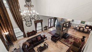 A spacious living area with a large chandelier, leather sofas, and a dining area with a high ceiling and large windows. - Mason Villa in Tampa (Tampa)