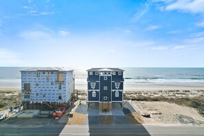 Dos edificios con vista al mar, uno en construcción y otro terminado, con una playa de arena y el océano al fondo.