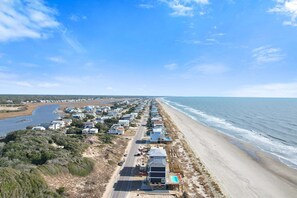 Zona residencial costera con casas a lo largo de la playa, una carretera y cielo despejado.